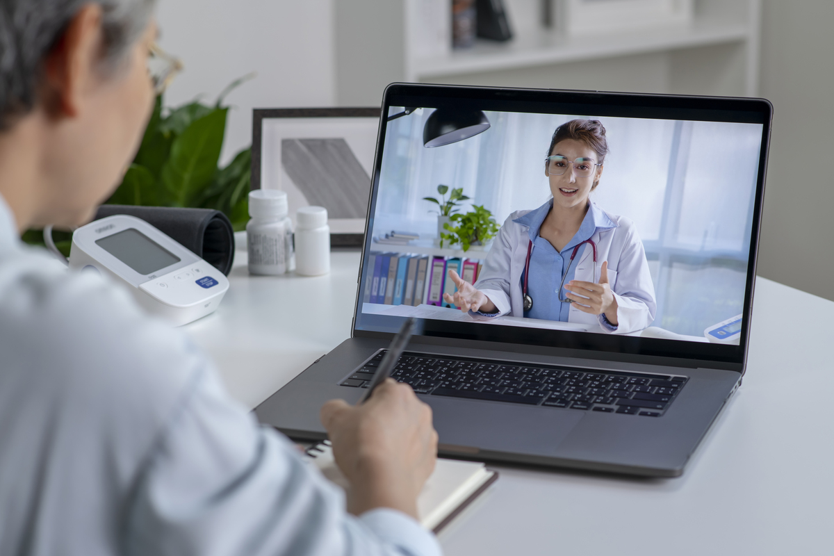 Mulher com laptop durante uma consulta online com seu médico em sua sala de estar, conceito de telemedicina
